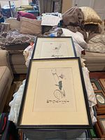 Two framed Asian-themed wall art pieces stacked, showing front glass and frames with visible scratches and beige matting.