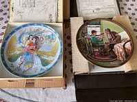Two collectible plates side by side; one from the Legends of West Lake series with a couple in traditional dress and a colorful phoenix, the other with a Norman Rockwell boy and grandfather illustration.