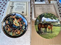 Two collectible plates displayed on table with associated certificates of authenticity; one plate depicts colorful Firebird legend artwork and the other a realistic horse and foal scene.