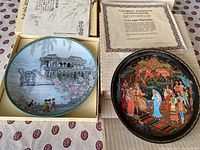 Two collectible plates with certificates, one depicting a Chinese building and garden scene, the other a Russian folk art scene, both in original boxes.
