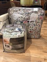 Two packaged bedding items displayed: a floral twin-size bedspread in a transparent plastic carrying case, and a folded fleece heated blanket in its original packaging.