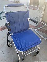 Foldable transport wheelchair fully open showing blue striped fabric seat and backrest, padded armrests, and lightweight metal frame with footrests.