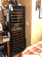 Full view of tall black wine fridge with glass door and wooden shelves inside.