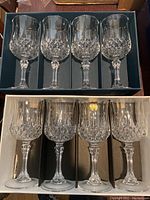 Two boxes each containing four Longchamp Cristal d'Arques crystal wine glasses with clear faceted stems and patterned bowls.