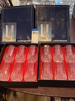 Two black boxes open showing total 12 crystal glasses, six in each box with red lining, diamond cut crystal design at base.