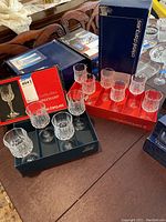 Two boxed sets of Longchamp Cristal d'Arques crystal glasses on a table. One box of 6 wine glasses and one box of 4 smaller glasses. Boxes have blue and red packaging with brand logos.