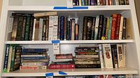 Two shelves filled with various books, including novels and biographies by different authors. Books are arranged standing upright and stacked horizontally in some places.