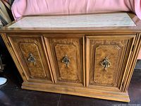Front full view of oak buffet cabinet with marble top showing wood grain, three doors with decorative paneling and metal handles, and base details.
