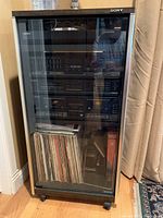 Full view of the Sony stereo system inside the wooden cabinet with glass door, showing all components stacked and vinyl records below.