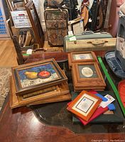 Still life framed painting of fruit and several framed pictures on a wooden table, showing most items included in the lot