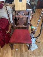 Full view of the wooden arm chair showing red seat cushion and ornate carved wood back and armrests.