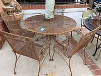 Photo showing vintage outdoor wrought iron round table and four matching chairs with umbrella. Details of table top, chairs, and rusted finish visible.