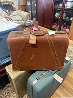 Front view of the vintage brown Platt Guardsman suitcase showing textured finish, handle, metal clasps, and attached luggage tag. Visible wear and scuffs.