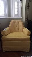 Yellow vintage low-back armchair with button tufting and matching cylindrical pillows shown near window and floor lamp