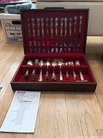 Full view of vintage silver-plated flatware set in wooden case with red velvet lining showing multiple spoons, forks and knives arranged neatly.