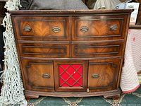 Full front view of vintage stereo cabinet with wood veneer, red speaker panel, and drawer fronts with metal pulls