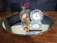 Ornate vintage vanity tray with mirror surface and gold edge, perfume bottle with bulb atomizer, and vintage clock.