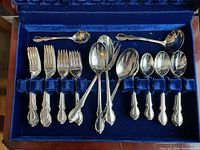 Photo of silverware pieces arranged in blue velvet lined storage box showcasing forks, spoons, and other utensils in the 1847 Rogers Bros Reflection pattern.