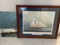 Photo showing both artworks, the original snowy scene painting unframed positioned behind the large framed Tim Thompson yacht print on carpeted floor.