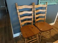 Photo showing two wooden ladderback chairs side by side against a gray wall.