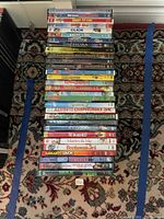Image showing a stack of 30 DVD cases arranged on a patterned carpet. DVD titles are family and kid-friendly movies such as Marley & Me, The Incredibles, Shrek series, Nacho Libre, and Bruce Almighty.