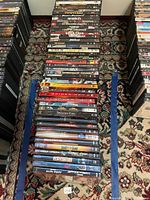 Photo showing two stacks of DVDs on patterned carpet with recognizable movie titles such as Spider-Man 1, 2, 3, Snatch, Tomb Raider 1 and 2, Dawn of Dead, Death Proof among others.