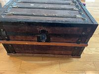 Top and front view of antique wood trunk with metal bands and latch lock, showing weathered and worn condition.
