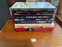Stack of six cookbooks on a wooden table showing spines with titles and authors