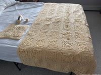Full view of the buttery yellow crocheted afghan laid on a bed with the matching small pillow cover and yarn skeins nearby.