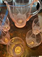 Close top view showing pink depression glass pitcher and several glasses with etched patterns and handle on pitcher