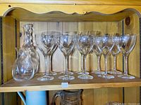 Kosta Boda Chateau glassware set displayed on wooden shelf showing 6 wine glasses, 4 smaller glasses, decanter, and small vase
