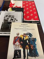 Photo showing Sotheby's Elton John costume and memorabilia catalogue with two large black and white promo photos and Rolling Stones Steel Wheels Tour program booklet in background