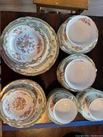 Top view of grouped china pieces showing diverse plate sizes, bowls, and cups with floral and gold trim design.
