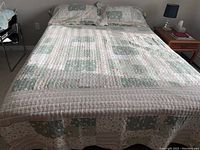 Full view of quilt spread on queen size bed with two matching pillow shams showing patchwork pattern in green, white, and floral accents.