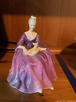 Front angled view of Royal Doulton Charlotte figurine showing a woman seated wearing a purple dress holding a small dog.