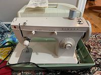 White Singer Model 247 sewing machine with power cord and accessories, placed inside a plastic carrying case.