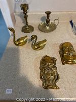 Photo showing two brass candle holders, two brass swan figures, and two brass Buddha face figures on a countertop.