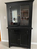 Front view of the black 2-piece wood hutch with glass upper doors and wooden lower cabinet, showing some wear and broken drawer handle.