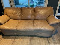 Front view of three-seater tan leather sofa showing cushions and armrests in leather, and pleather base and sides.
