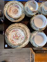 Full view of assembled china pieces showing plates, bowls, cups and saucers with floral patterns and gold accents.