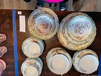Top-down photo of stacked plates, cups and saucers showing floral Noritake Tremont pattern with gold accents