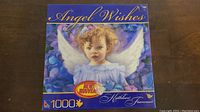 Box top showing image of curly-haired angel child with white wings surrounded by purple and blue flowers, title 'Angel Wishes', puzzle piece count 1000.