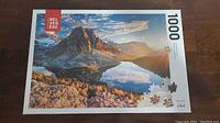 Box cover of 1000-piece jigsaw puzzle showing Canadian mountain and lake scenery under a clear sky with some clouds and autumn trees.
