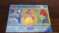 Box top showing the puzzle image with Disney Princesses Cinderella, Belle, and Ariel. It specifies 200 pieces and is made by Ravensburger.