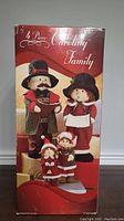 Box showing full 4 piece caroling family figurine set with adult and children figures