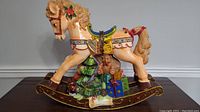 Side view of the Christmas rocking horse showing detailed painting and holiday decorations including holly, presents, teddy bear, and musical instrument.