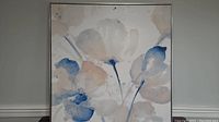 Front-facing photo of the framed floral watercolor artwork showing the soft blue, beige, and gray flower shapes on a light background with a thin dark frame.