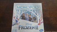 Front box displaying the Monopoly Frozen II logo and main characters Olaf, Anna, Elsa, and Sven on a winter forest background.