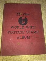 Front cover of 'The New World Wide Postage Stamp Album' in red hardcover with title text and illustration.