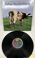 Front cover of Pink Floyd Atom Heart Mother showing cow on green field beneath blue sky.
